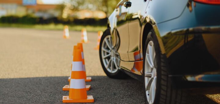 Car parked in a parking lot with orange and white traffic cones set up in a row beside it, reflecting off the car's surface.