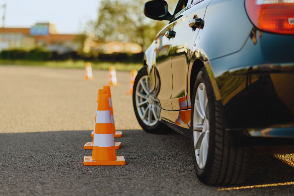 777944 - Autoescuela Isabel Segunda | ComunicaTech.Com Car parked in a parking lot with orange and white traffic cones set up in a row beside it, reflecting off the car's surface.