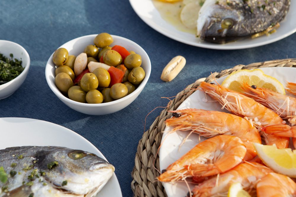 Shrimp platter with lemon wedges, olives, and other seafood dishes on a blue table.