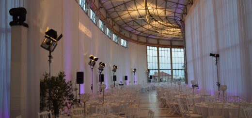 Detrás de cada evento exitoso existe un equipo de planificación especializado - Elegant banquet hall set for a formal event with round tables, white chairs, and purple uplighting.