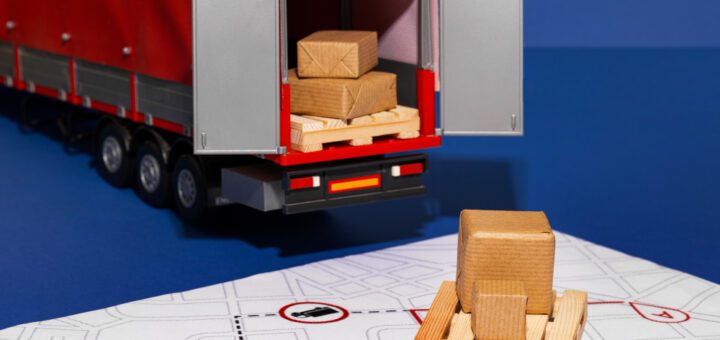 Toy red trailer truck with open back doors, boxes on a pallet next to a printed map layout.