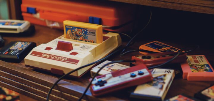 Vintage Nintendo Family Computer (NES) with a cartridge inserted, surrounded by colorful game cartridges on a wooden shelf.