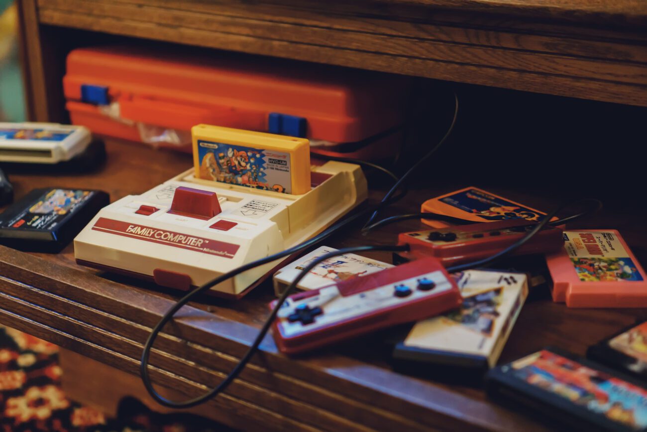 Vintage Nintendo Family Computer (NES) with a cartridge inserted, surrounded by colorful game cartridges on a wooden shelf.