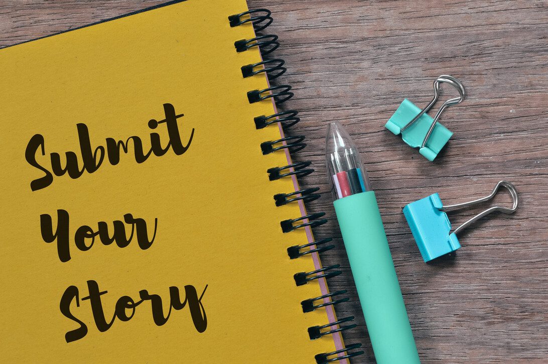 Top view of pen paper clips and notebook written with SUBMIT YOUR STORY | ComunicaTech.Com Yellow notebook with 'Submit Your Story' beside a teal pen and binder clips on a wooden desk.